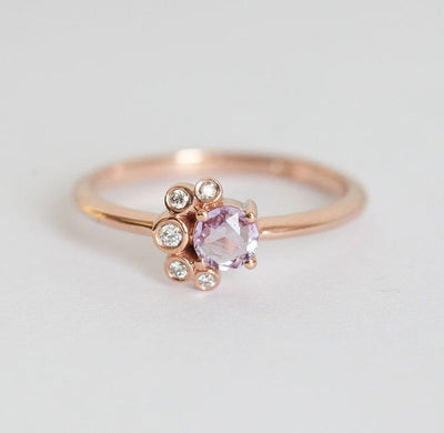 Nahaufnahme eines runden Saphir-Diamant-Clusterrings mit rosa Saphir, weißen Diamanten und Goldband.