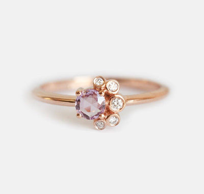 Nahaufnahme eines runden Saphir-Diamant-Clusterrings mit rosa Saphir, weißen Diamanten und Goldband.