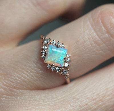 Quadratischer Opal-Halo-Ring mit runden weißen Diamanten im Prinzessschliff, die den zentralen Edelstein umgeben