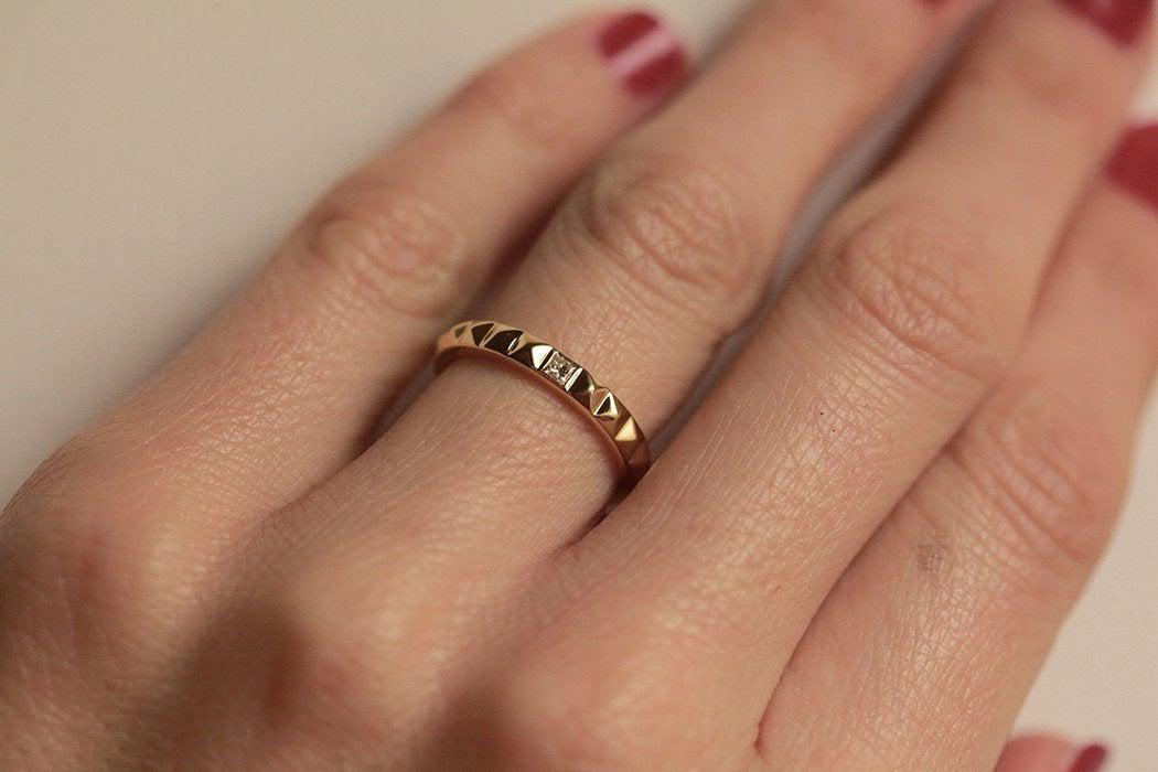 Ein goldener Ring mit Pyramidenstruktur und einem weißen Diamanten im Prinzessschliff