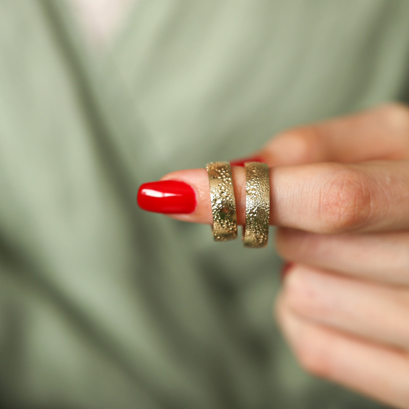 Strukturierter goldener Ehering an einem Finger mit roten Nägeln und goldenen Ringen. Unisex-Twist-Design aus 14-karätigem und 18-karätigem Gold.