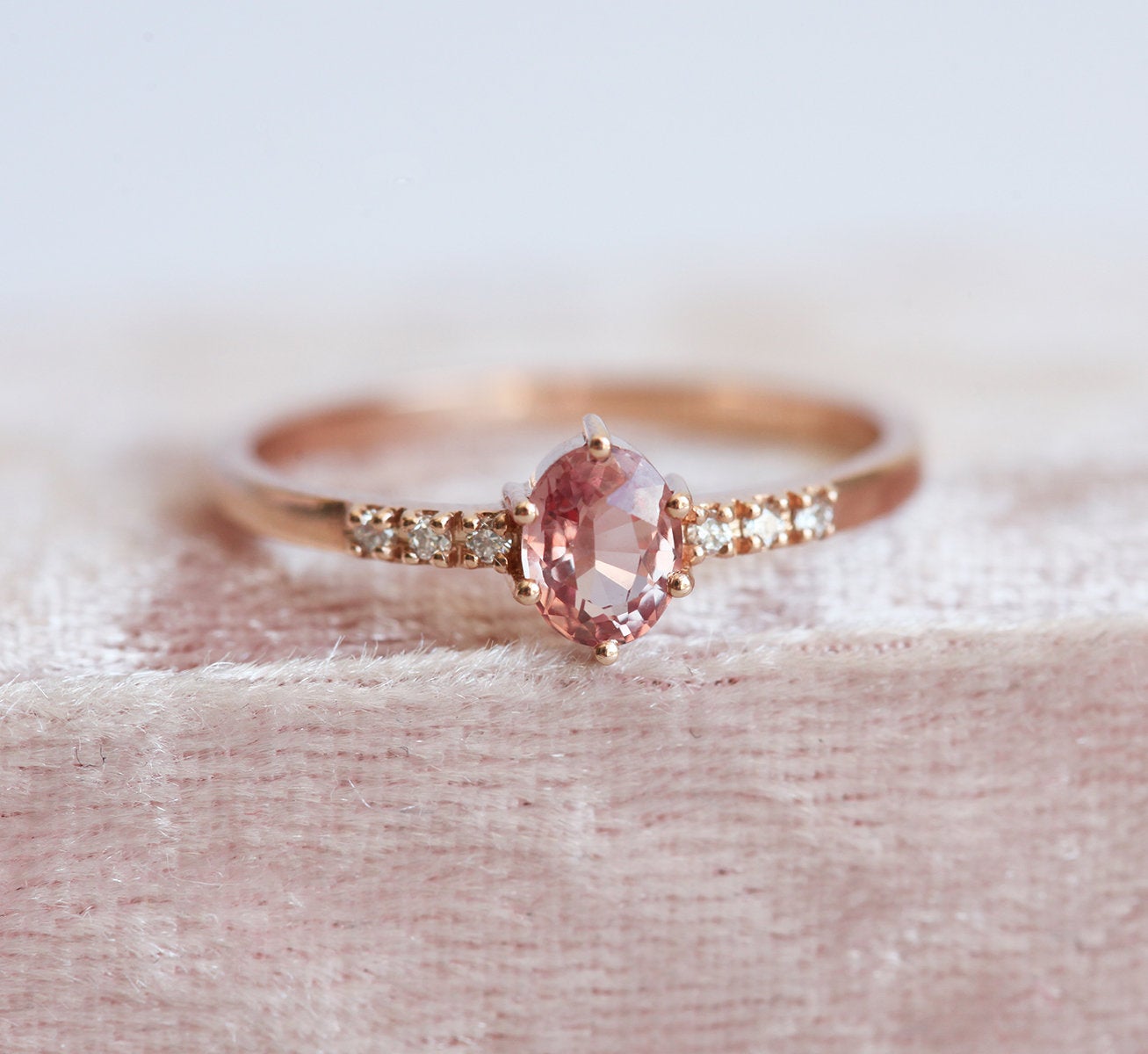 Ovaler pfirsichfarbener Padparadscha-Saphirring mit weißen Diamanten an der Seite