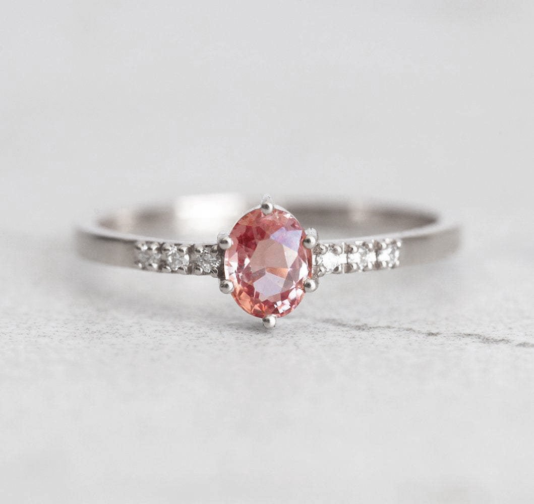 Ovaler pfirsichfarbener Padparadscha-Saphirring mit weißen Diamanten an der Seite