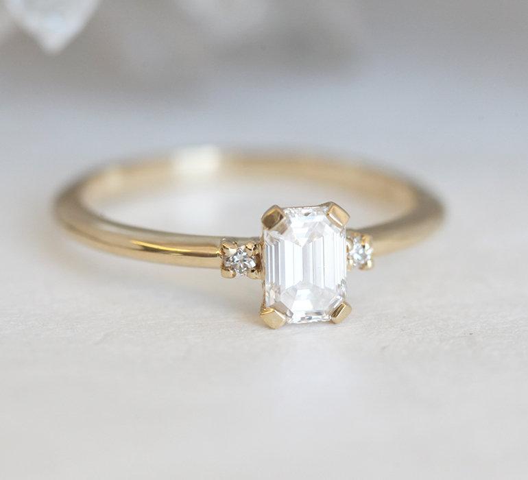 Diamantring im Smaragdschliff mit seitlichen Diamanten aus 14 Karat Gelbgold, der Eleganz und Brillanz unterstreicht.